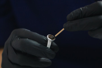 Hands in black gloves are typed mixed with a wooden stick a pigment ring with a single cup of paint for microblading eyebrows close-up.