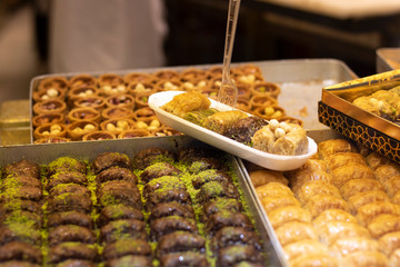 Baklavar is put in plastic plates in various flavors and has a plastic fork on it. It was taken in front of the market.