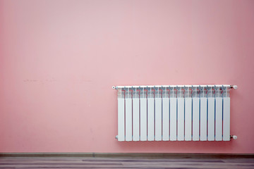 home gas heater closeup .Heating radiator on a pink wall at an apartment. Modern living room. Radiator in room. Heating system . Heating radiator in a white room with laminated wooden floor .