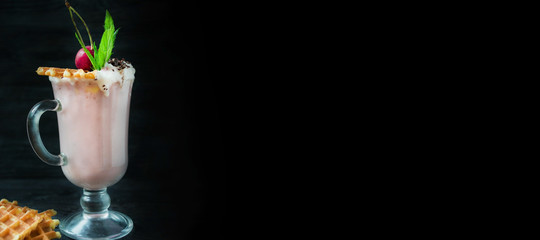 Cherry milkshake with ice cream and whipped cream, marshmallows, cookies, waffles, served in a glass cup on a dark background. Summer drink. Banner. Space for text.