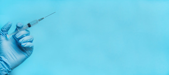 A hand in a blue glove holds a syringe. The doctor holds a syringe for vaccination. Medicine. Blue benner background, place for text. Copy space.