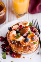 Delicious and lush pancakes with fresh fruits and berries, poured with salted caramel. Mint, tea, orange juice, milk on the table.