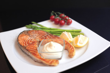 salmon steaks with vegetables and spices: asparagus, tomatoes, ginger, pepper corns, salt, chili, onion, lemon and olive oil on black background. Healthy food diet concept. Top view.