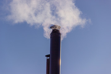 Smoke from the chimney, heating the house in winter..Chimney stacks made of metal with smoke coming up..Smoke in the blue sky..