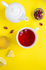 Obraz na płótnie Canvas Herbal tea with pink roses in the white cup on the yellow background. Location vertical. Top view. Copy space.