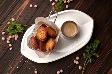Chickpea  flafel with sauce, on a white plate, on a wooden board. Chickpeas and herbs around the plate