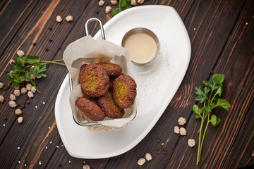 Chickpea  flafel with sauce, on a white plate, on a wooden board. Chickpeas and herbs around the plate