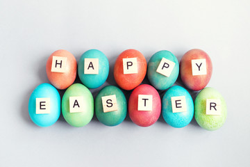 Text HAPPY EASTER made from wooden letters and bright multi-colored Easter eggs on a gray background, top view. Easter background.	