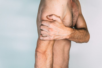 Caucasian man without shirt with hand on triceps, isolated on white background, pain concept