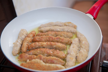 The long cutlet is fried in a red pan. She cooks the cutlet in a white pan.