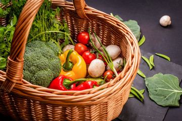 Vegetarian vegetables: mushrooms, peppers, broccoli, tomatoes, herbs in a wicker basket on a black background in the studio