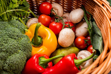 Vegetarian vegetables: mushrooms, peppers, broccoli, tomatoes, herbs in a wicker basket on a black background in the studio