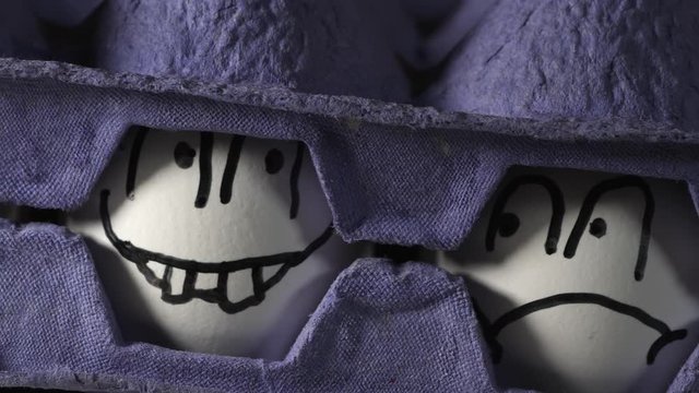 The white eggs with drawn faces in between two blue trays