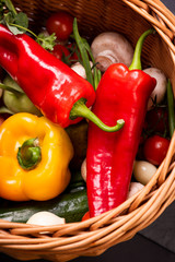 Vegetarian vegetables: mushrooms, peppers, broccoli, tomatoes, herbs in a wicker basket on a black background in the studio