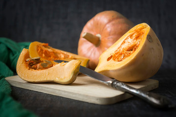Beautiful ripe pumpkins against a dark background, sliced and whole.