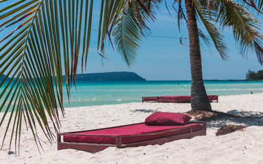 Obraz na płótnie Canvas A bed at the beach under a plam tree