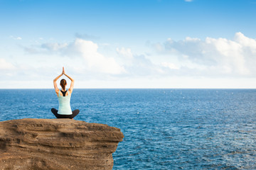 Young woman mediating on a cliff by the waters edge. . 