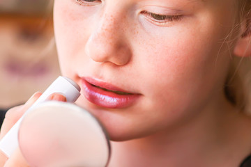 Young attractive teenager girl's face view with makeup. Girl putting lipstick