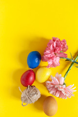 Colorful easter eggs with bright colorful spring flowers on the yellow background. Top view. View from directly above. Spring festive holidays background. Vertical image