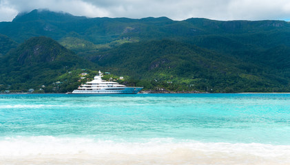 Fototapeta premium View at amazing tropical beach with beautiful white sand ,crystal blue ocean and luxury white yacht with island at background. Space for text