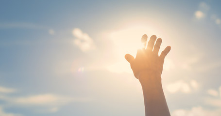 Naklejka na ściany i meble Hand reaching up touching the sun sunset sky with rays of light shinning through fingertips, 