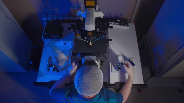 In a Modern Laboratory Scientist Conduct Experiments. Chief Research Scientist Adjusts Specimen in a Petri Dish and Looks on it Into Microscope.