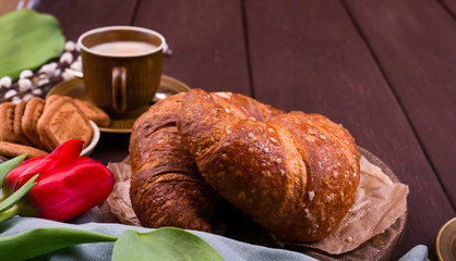 Easter breakfast with aromatic fresh espresso, croissants, colored eggs, red tulips and willow. Coffee with pastries, flowers on a wooden table. View from above. Copy space.
