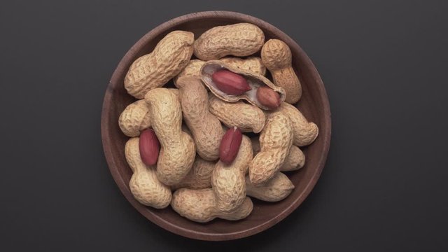 Bunch of peanuts in bowl rotating on dark gray background. Top view Close up. Arachis hypogaea