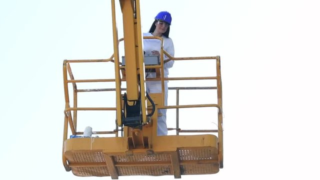 Woman in safety gear lowers the platform of a telescopic boom lift using the control panel in slow motion. Work concept.