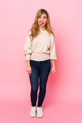 Young blonde caucasian woman standing over a pink background funny and friendly sticking out tongue.