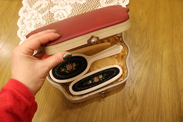 A woman's hand in a red sleeve opens a vintage red box with a set of beautiful brushes that stands...