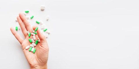 Palm hand full of white and green scattering pills. Capsules with medicines on light background. Flat lay, top view.