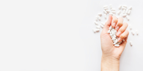 Palm hand full of white scattering pills. Woman gripes hand with capsules with medicines on light background. Flat lay, top view. Banner with copy space.