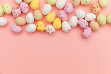 Happy Easter concept. Preparation for holiday. Easter candy chocolate eggs and jellybean sweets isolated on trendy pastel pink background. Simple minimalism flat lay top view copy space.