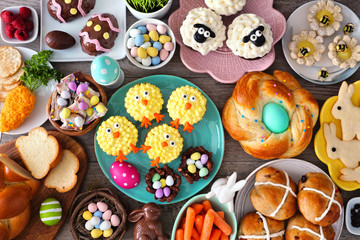 Easter table scene with an assortment of breads, desserts and treats. Top view over a wood...