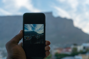 Close of a  hands holding a mobile phone with view of Table Mountain from Bo-Kaap or Malay in background