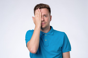 Caucasian casual man closes one eye hand, passing through eyesight test