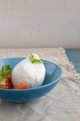 Large mozzarella with slices of tomatoes and basil in a blue plate. Rustic style.