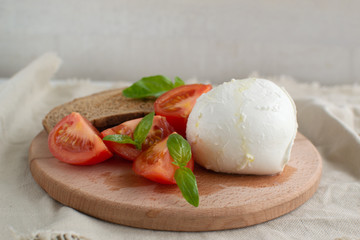 Large mozzarella with slices of tomatoes and basil on a wooden cutting board. Rustic style.