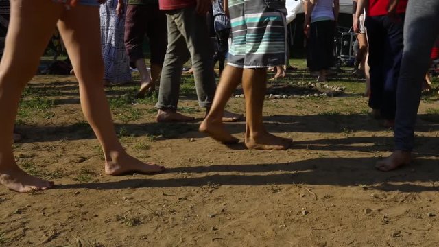 Closeup of legs of a group of similar community men and woman walking barefoot in park during guided cacao ceremony at evening