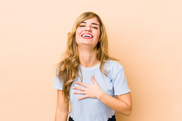 Young blonde caucasian woman laughs out loudly keeping hand on chest.