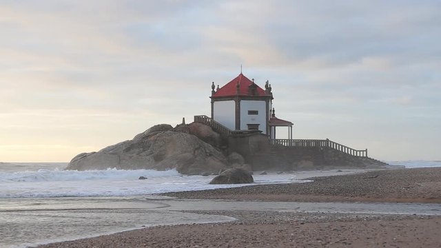 Beautiful church at the beach. Capela Senhor da Pedra, at sunset, with waves crashing over the church