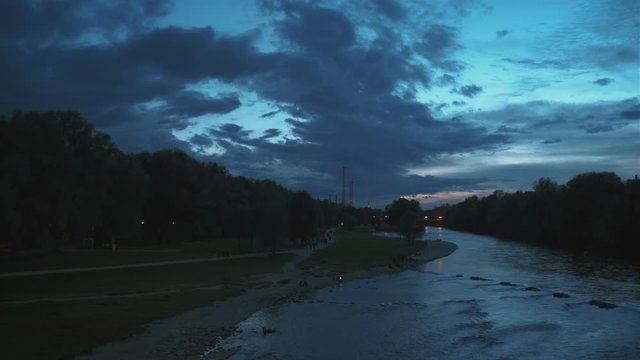 Munich nature at dramatic dusk: autumn in park of tourist Bavarian city. View of Isar river, trees and St Maximilian church from Reichenbach Bridge. Munchen, Bavaria, Germany. Camera horizontal pan