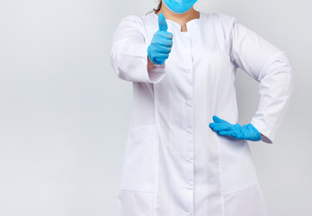 medic woman in white coat and mask, wearing blue medical latex gloves on her hands, showing like gesture in hand