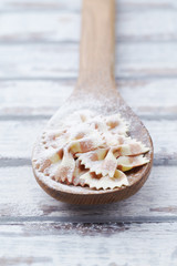 Fototapeta na wymiar Farfalle pasta on wooden spoon. Bright wooden background. Close up. 