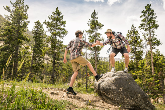 Father and son balance and stand on rock triumphantly while hiking in the mountains. Greenough Lake,  Montana, USA