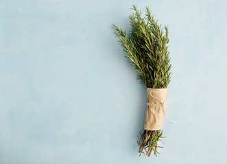 A bunch of fresh green twigs of rosemary wrapped in paper and tied with a rope lies on a blue...