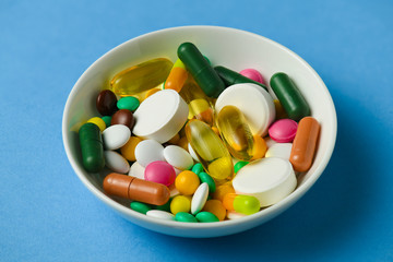 A dish full of pills, tablets, vitamins, drugs, omega 3 fish oil, gel capsules, medicament and food supplement for health care. Blue background.