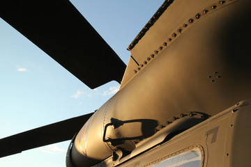 bottom view of a olive drab military helicopter with propeller blades against a blue sky