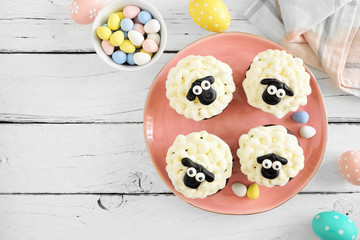 Cute Easter sheep cupcakes. Above view table scene with a white wood background.